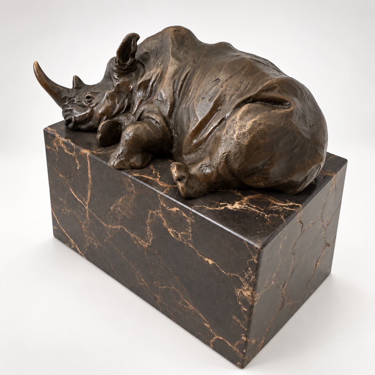 Liegendes Nashorn aus Bronze auf dunklem Marmorsockel in schräger Ansicht
