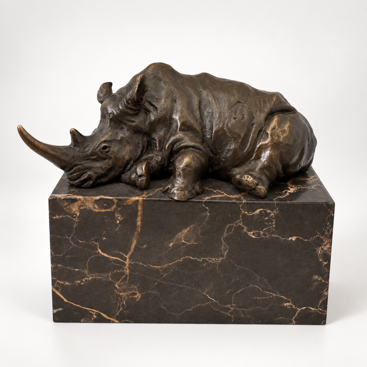 Liegendes Nashorn aus Bronze auf dunklem Marmorsockel in schräger Ansicht von links