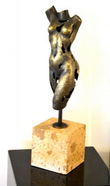 Abstrakter Frauentorso aus Bronze in beleuchteter Gesamtansicht mit Metallhalterung und kubischem Steinsockel auf dunklem Podest.