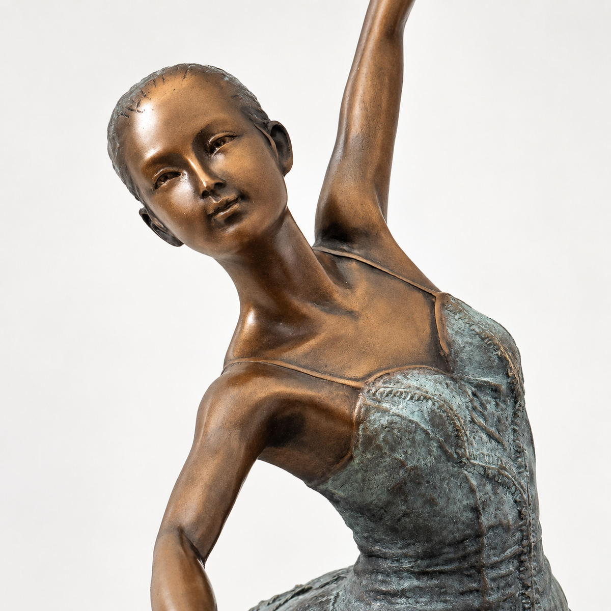 Nahaufnahme von Gesicht und Oberkörper der Bronze-Ballerina mit warmen Bronzetönen und grün patiniertem Ballettkleid.