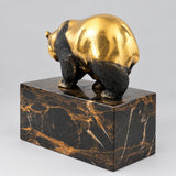 Bronzebär auf dem dunkel marmorierten Sockel in rückwärtiger Schrägansicht.