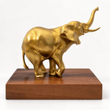 Seitenansicht der goldfarbenen Bronzefigur Elefant mit nach oben geschwungenem Rüssel und rechteckigem Sockel.