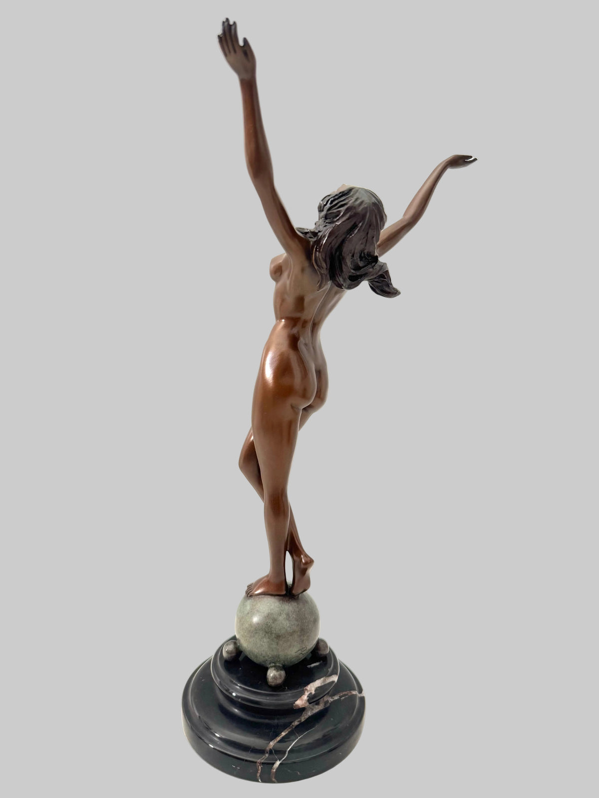 Schräge Rückansicht der Bronzefigur Frau von Raymondo mit erhobenen Armen auf türkisfarben patinierter Kugel.
