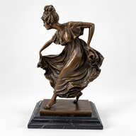 Bronzefigur einer Tänzerin mit schwingendem Kleid auf schwarzem Marmorsockel, schräg von vorn.
