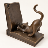 Katze aus Bronze mit Brille neben der aufgerichteten Buchseite links, mit Blick auf die gravierte Buchfläche.