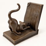 Katze aus Bronze mit Brille und geschwungenem Schwanz, daneben rechts die aufgerichtete Buchseite mit Gravuren.