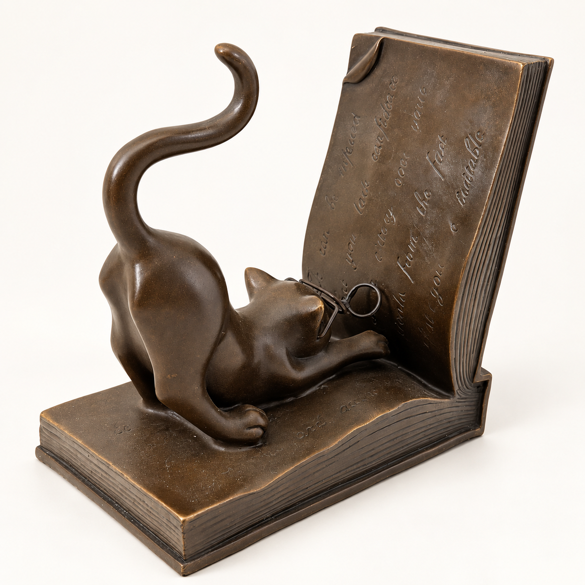 Katze aus Bronze mit Brille und geschwungenem Schwanz, daneben rechts die aufgerichtete Buchseite mit Gravuren.